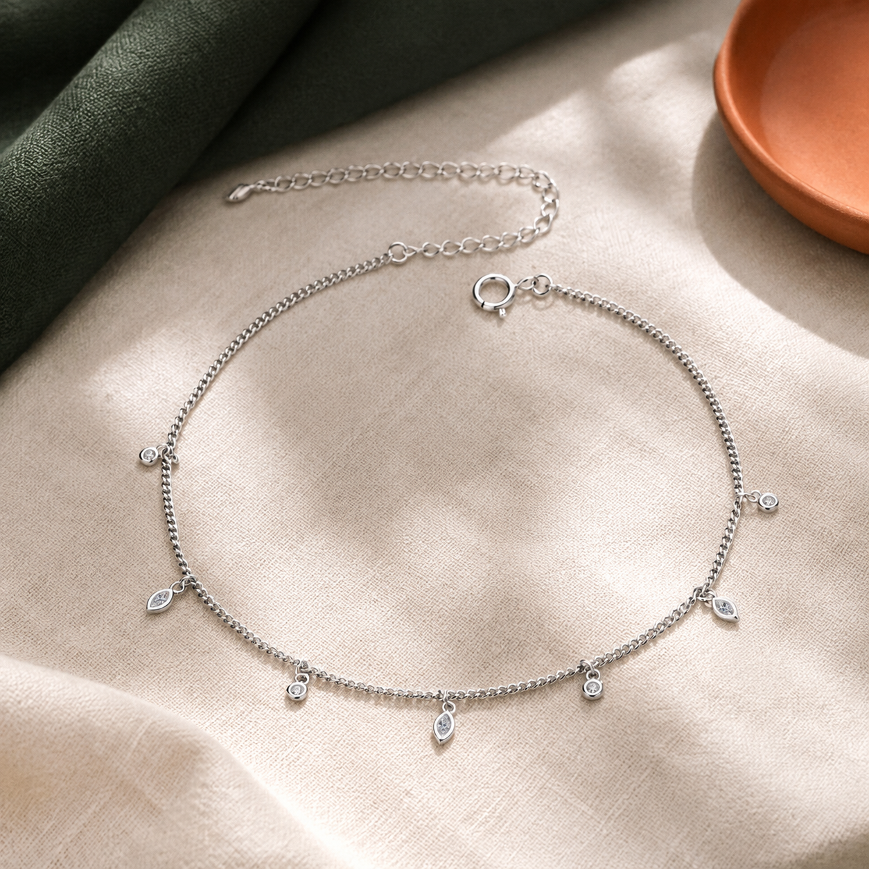 Delicate silver charm anklet arranged on ivory linen