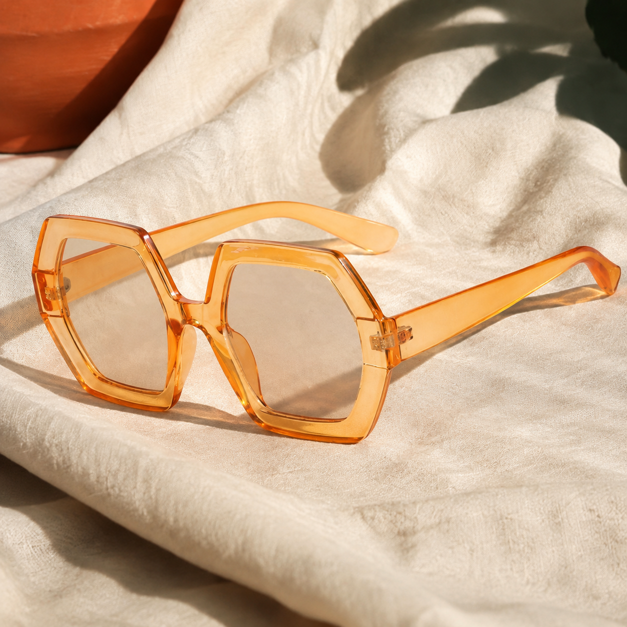 Translucent orange polygon sunglasses on ivory linen
